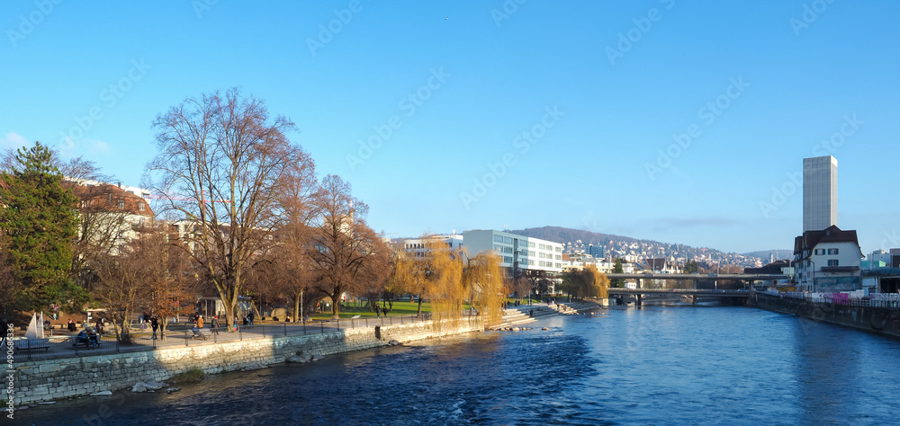 Zurich, Switzerland - December 18th 2021: People enjoying autumnal colours and sunlight in a park at the Limmat river