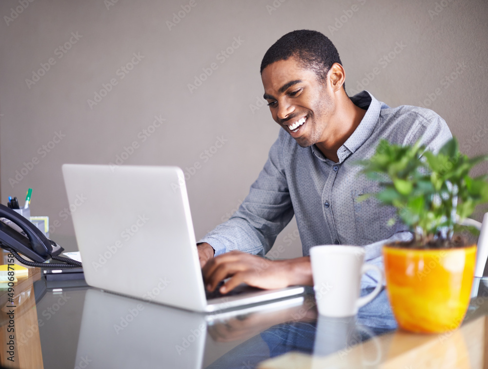 One of those days where everything goes smoothly. Shot of a handsome young man happily working on his laptop at home. One of those days where everything goes smoothly. Shot of a handsome young man happily working on his laptop at home.