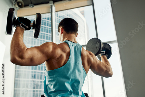 Athletic man shakes his biceps with dumbbell in his hands. Healthy lifestyle concept