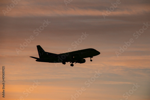 The plane comes in to land at the airport against the background of dawn. Passenger airliner flying at low altitude with landing gear released against the background of dawn