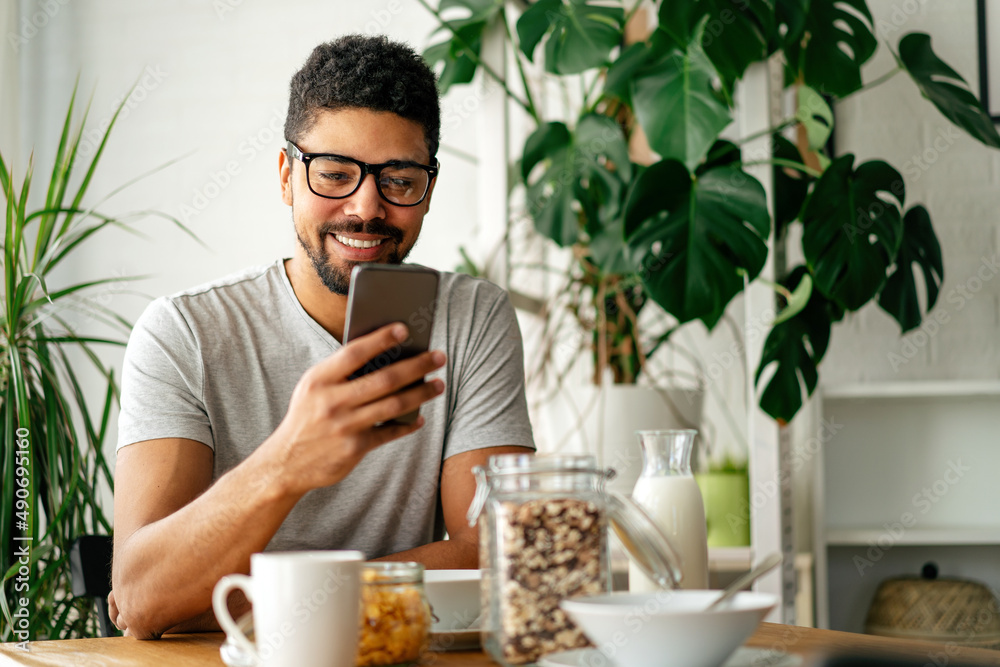 Young black man eating breakfast and reading the news online. Handsome man using mobile phone Young black man eating breakfast and reading the news online. Handsome man using mobile phone