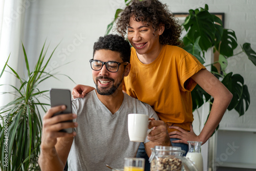 Joyful couple smiling and taking selfie on cellphone while having breakfast at home