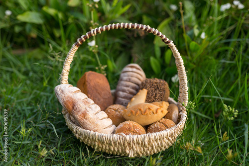 Assorti of brown and white homemade bread in wicker basket standing on the grass