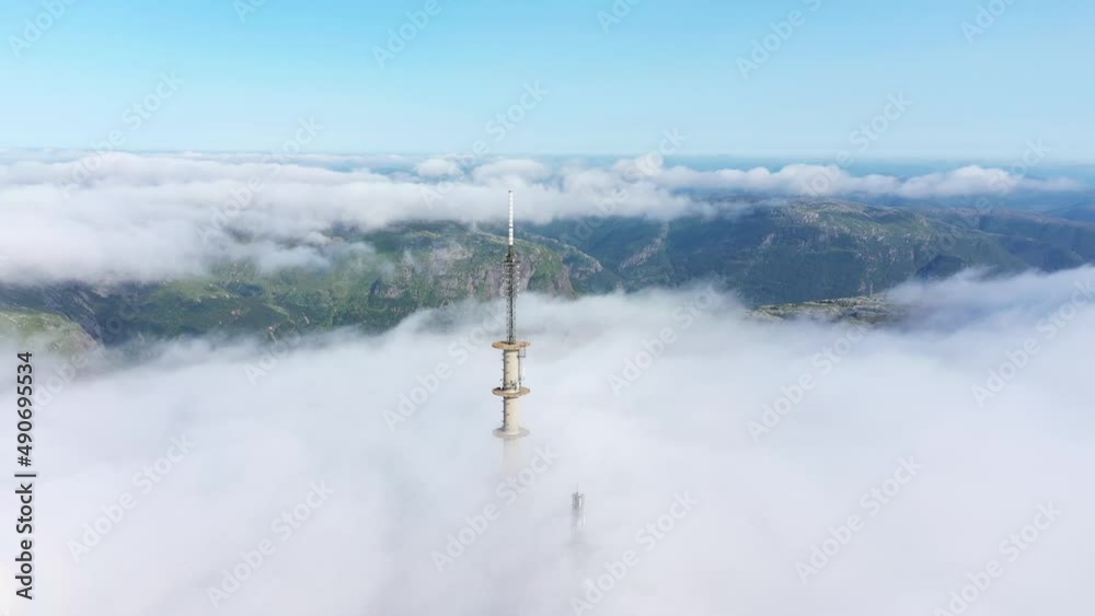 circling radio tower above clouds with mountains revealed beneath