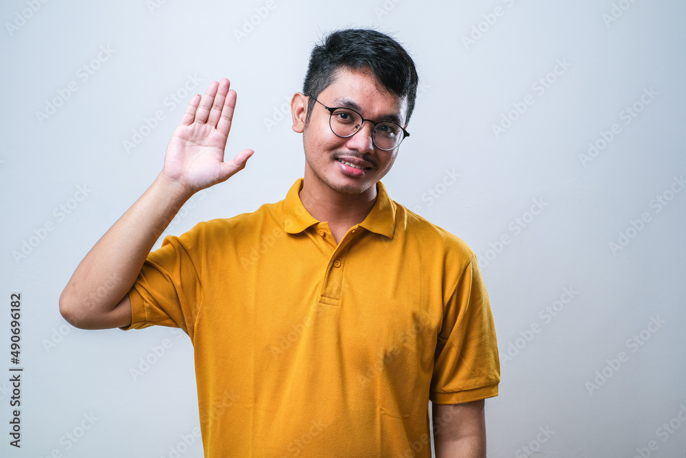 Young handsome asian boy waiving saying hello happy and smiling, friendly welcome gesture Young handsome asian boy waiving saying hello happy and smiling, friendly welcome gesture