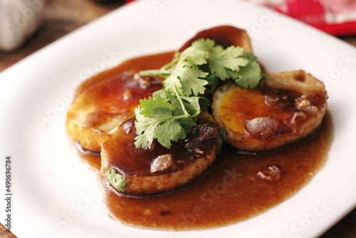 Egg with Tamarind Sauce in a white plate served on a wooden table with coriander sprinkles, is a popular local dish that Thai people eat.