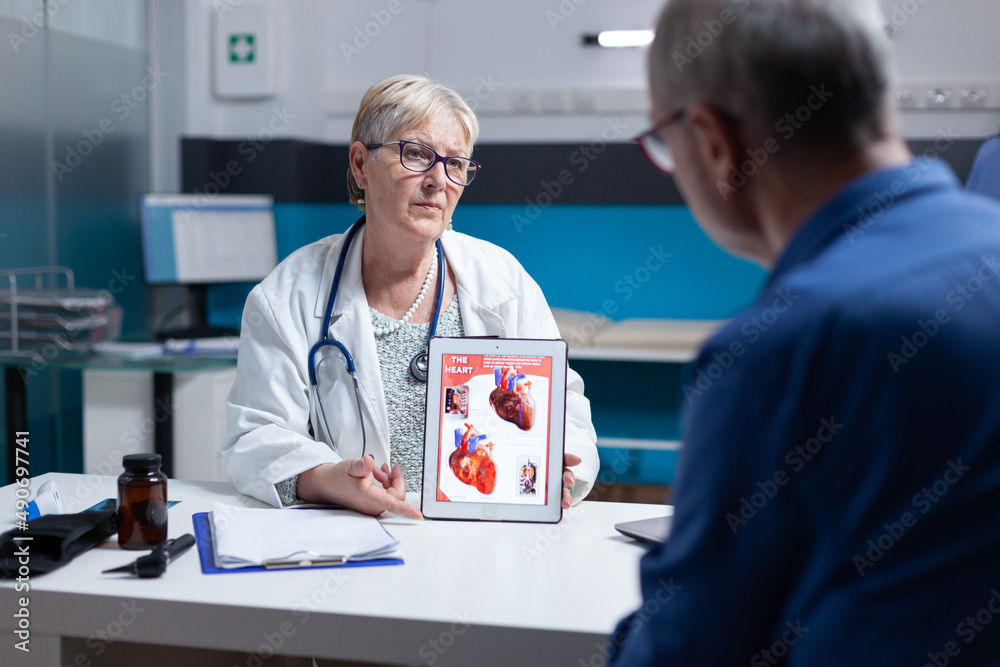 Obraz premium Physician explaining cardiology diagnosis with image of heart organ on tablet to patient. General practitioner showing illustration on cardiovascular system and anatomical structure to man.