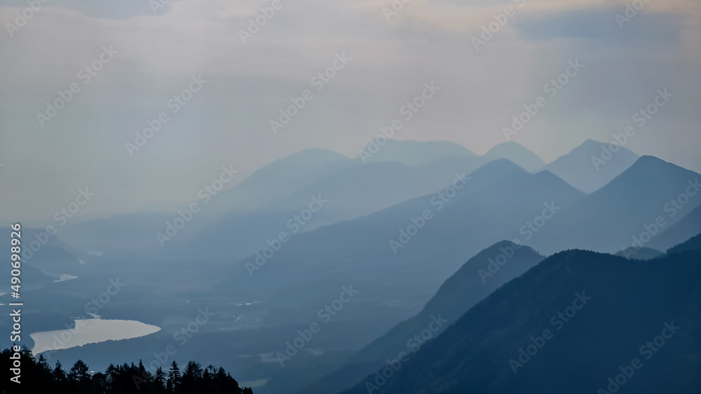 Obraz premium Scenic view on the alpine mountain chains of the Karawanks in Carinthia, Austria. Peaks are shrouded in morning fog. Mystical vibes. Clear and sunny day. Serenity. View from Ferlacher Spitze, Alps