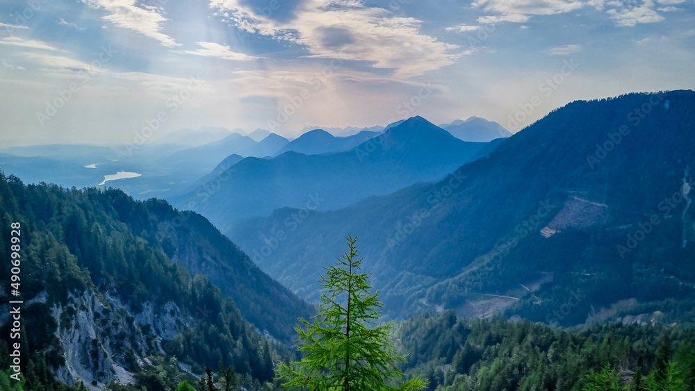 Scenic view on the alpine mountain chains and woodland of the Karawanks in Carinthia, Austria. Peaks are shrouded in morning fog. Mystical vibes. Ssunny day. Serenity. View from Ferlacher Spitze, Alps