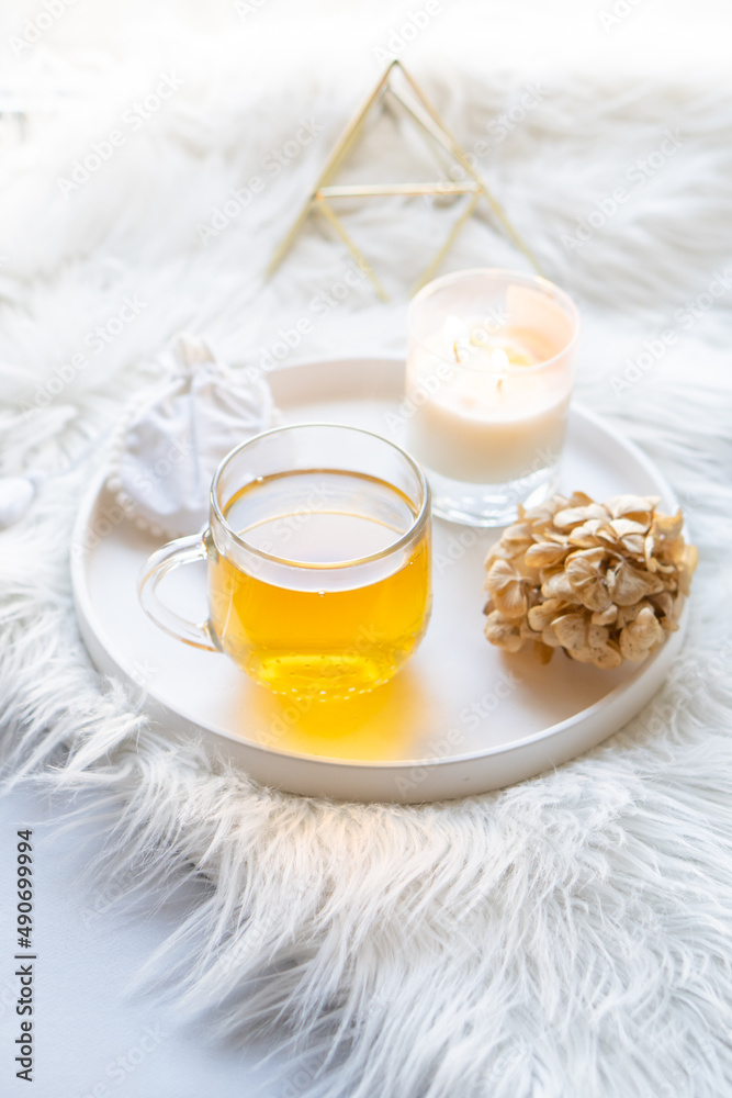 Cup of herbal tea and burning candle on round white decorative tray