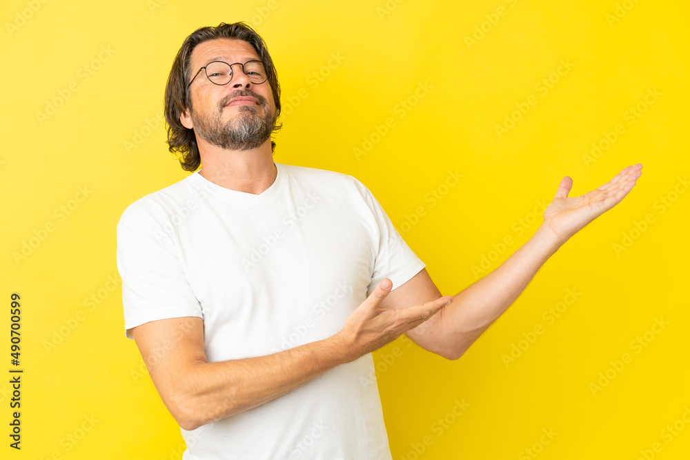 Senior dutch man isolated on yellow background extending hands to the side for inviting to come Senior dutch man isolated on yellow background extending hands to the side for inviting to come