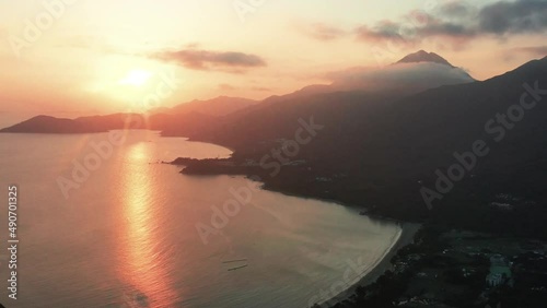 Aerial truck left of sea and Pui O beach bay near village and rainforest hills at golden hour with sunbeams, Lantau Island, Hong Kong, China photo