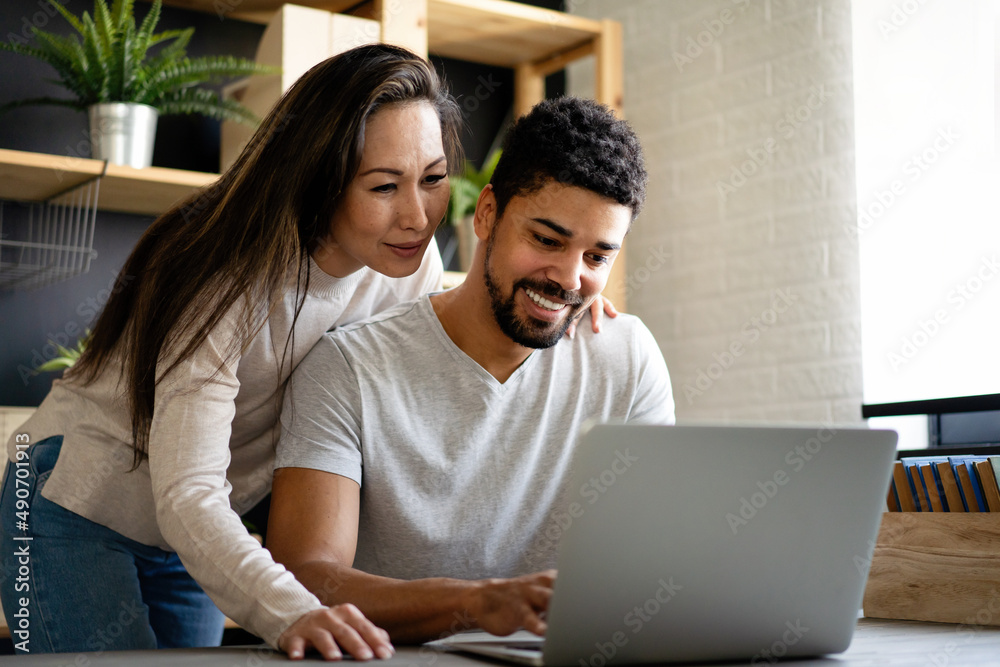 Happy interracial couple smiling while working or having fun at laptop Happy interracial couple smiling while working or having fun at laptop