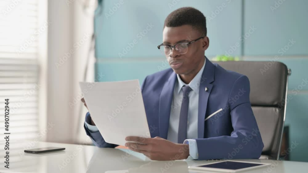 Young African Businessman Upset while Reading Documents in Office Young African Businessman Upset while Reading Documents in Office