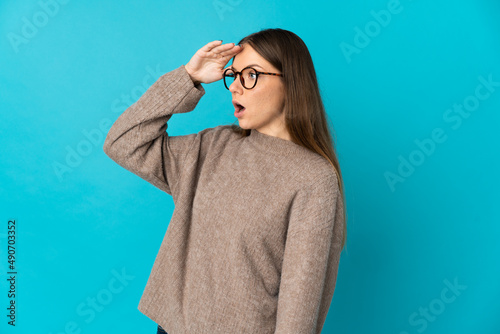 Young Lithuanian woman isolated on blue background with surprise expression while looking side