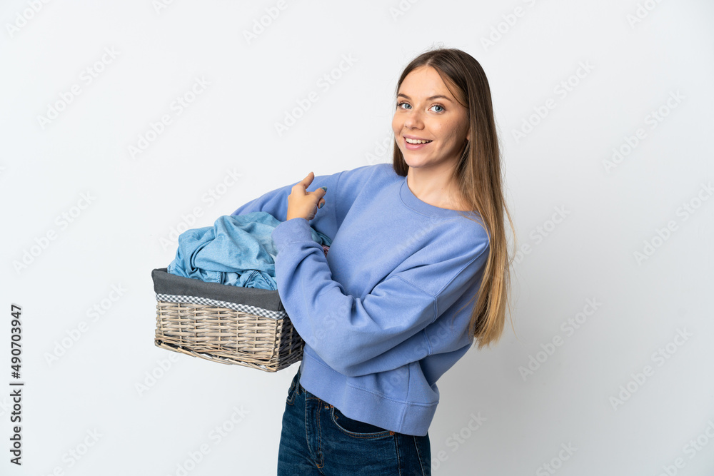 Young Lithuanian woman holding a clothes basket isolated on white background pointing back