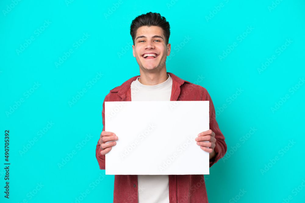 Young handsome caucasian man isolated on blue bakcground holding an empty placard with happy expression Young handsome caucasian man isolated on blue bakcground holding an empty placard with happy expression