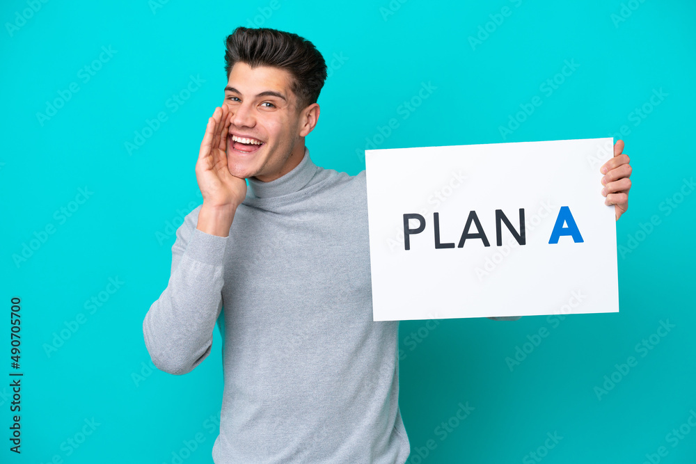 Young handsome caucasian man isolated on blue bakcground holding a placard with the message PLAN A and shouting Young handsome caucasian man isolated on blue bakcground holding a placard with the message PLAN A and shouting