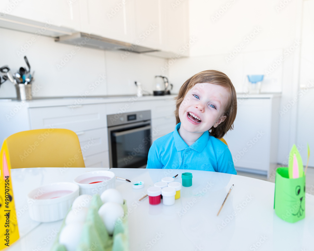Easter, a little boy happily preparing to paint eggs, in front of him is a homemade bunny made of paper Easter, a little boy happily preparing to paint eggs, in front of him is a homemade bunny made of paper