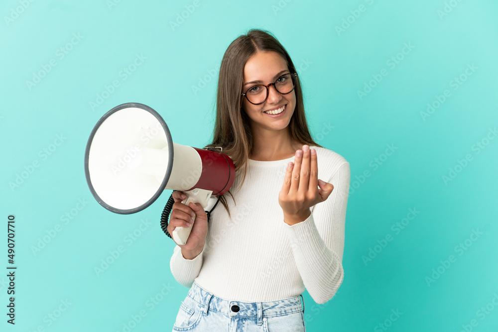 Young woman over isolated blue background holding a megaphone and inviting to come with hand Young woman over isolated blue background holding a megaphone and inviting to come with hand