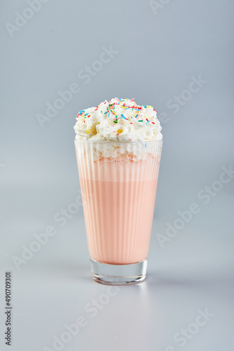 Pink milkshake with whipped cream and colored sugar sprinkles on gray background