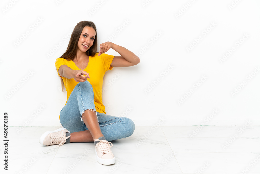 Young girl sitting on the floor points finger at you while smiling