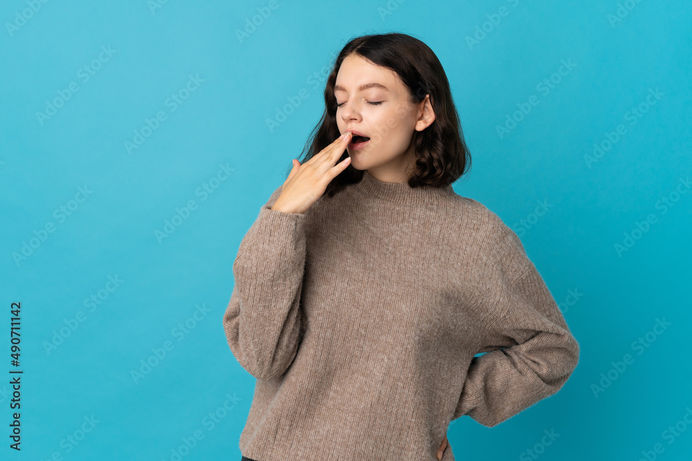 Teenager Ukrainian girl isolated on blue background yawning and covering wide open mouth with hand