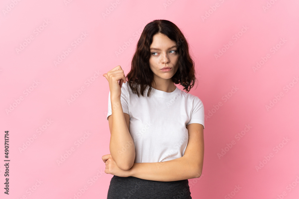 Teenager Ukrainian girl isolated on pink background unhappy and pointing to the side Teenager Ukrainian girl isolated on pink background unhappy and pointing to the side