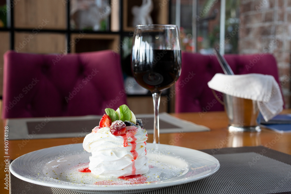 Pavlov dessert with whipped whites and berries and a glass of red wine in the restaurant. Pavlov dessert with whipped whites and berries and a glass of red wine in the restaurant.