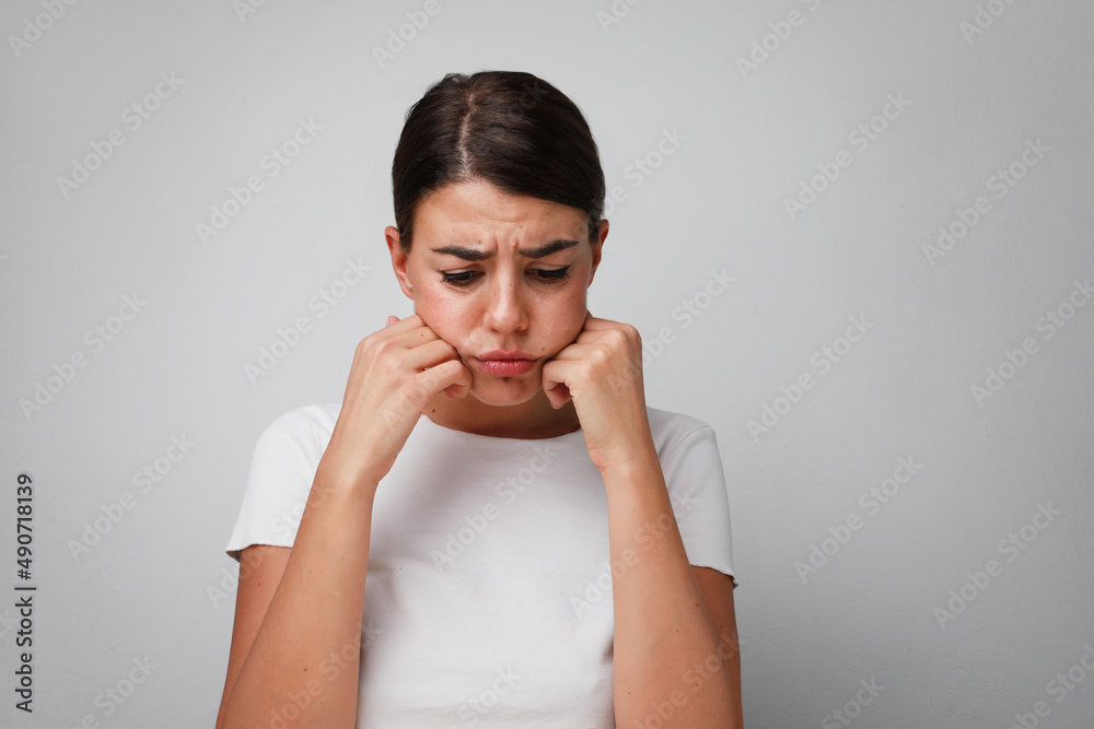 Woman with sad face expression posing on white wall in the studio. Isolated. Woman with sad face expression posing on white wall in the studio. Isolated.