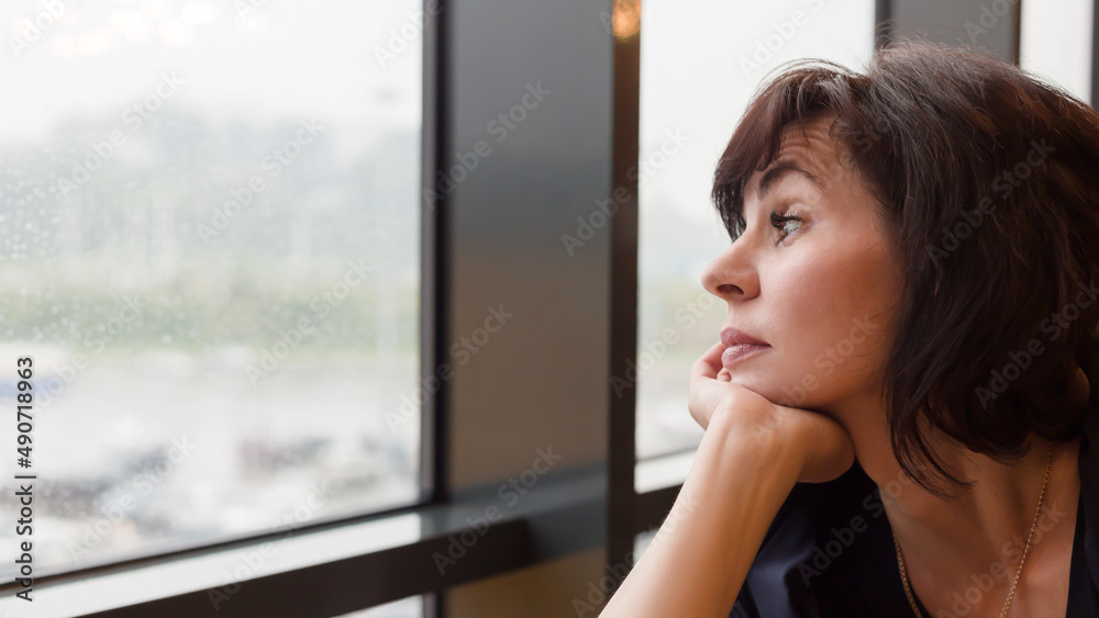 Woman 35-40 years old sadly looks at rain outside window, Woman 35-40 years old sadly looks at rain outside window,