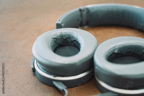 full-sized gray headphones with deformed and damaged leather material on the earcups on a wooden table
