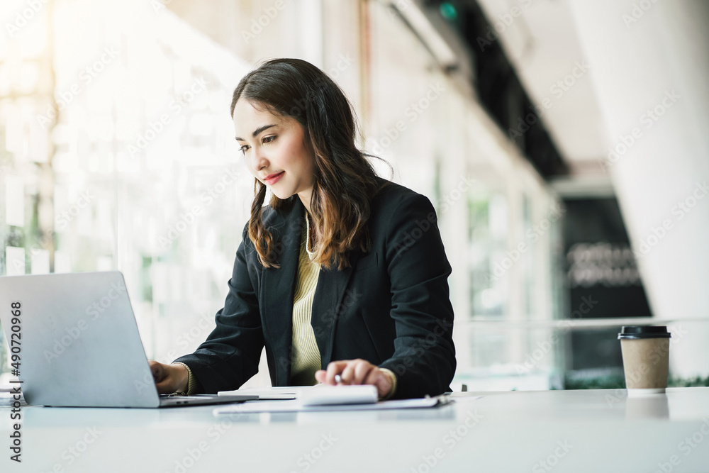 Portrait of a beautiful Asian woman looking at laptop screen while sitting at working desk in the office. Portrait of a beautiful Asian woman looking at laptop screen while sitting at working desk in the office.