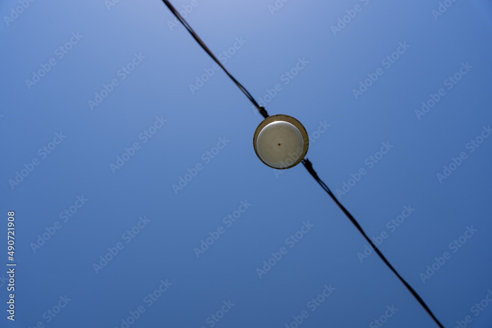 a blue sky whose black electric cable with a lantern divides it diagonally into two parts. a blue sky whose black electric cable with a lantern divides it diagonally into two parts.