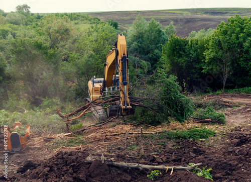 Yellow excavator with bucket clearing vegetation in rural region in Bulgaria in summer sunny day