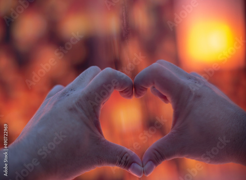 Made hand in the shape of a heart with a mirror with blurred orange background.
