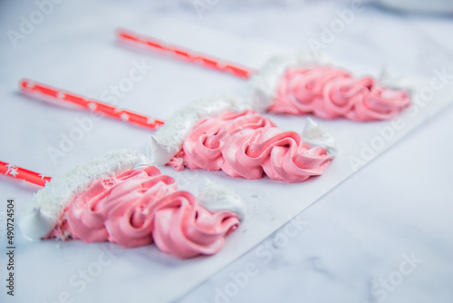 Meringue in the form of pink Christmas hats, with a white bumbone and rim lies on white parchment. High quality photo photo