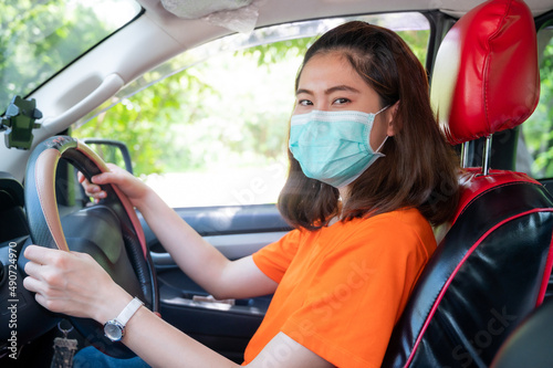 Young Asian woman wearing surgical mask for prevent the spread of coronavirus while driving car. Conceptual of new normal lifestyle of people after covid-19 pandemic.