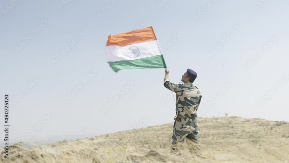 full shot Indian army soldier holding waving Indian flag on top of mountain - concept of independence or repubilc day celebration, patriotisms and freedom