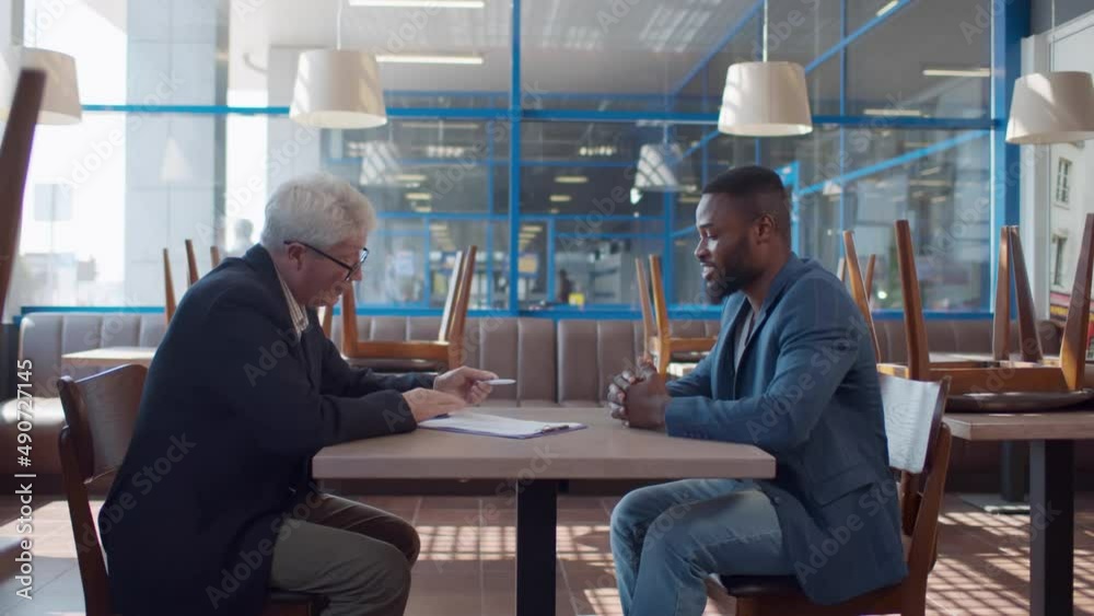 Side view of business partners sign contract and shake hands in empty restaurant. Realtime Side view of business partners sign contract and shake hands in empty restaurant. Realtime