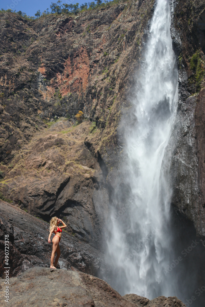 blonde girl on a large rock under a huge waterfall in Australia