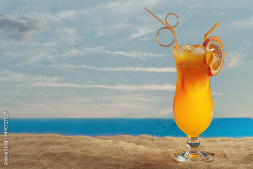 Orange cocktail on the beach. Alcoholic drink with ice, orange on the sand close up. Sunset, sea and sky in the background. Copy space and free space for text near the glass.