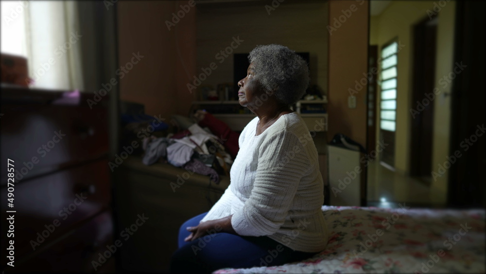 A pensive senior woman sitting by bedside at home in contemplation