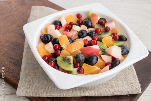 Fruit sliced homemade diet breakfast salad of apples, tangerines, kiwis, grapes, cranberries and blueberries in a white bowl. 