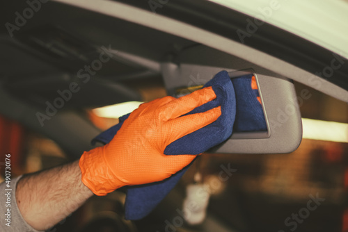 Detailing and car cleaning services the concept of car washing and cleaning.A male worker in orange rubber gloves  cleaning the plastic of the car interior with a blue microfiber towel.Auto detailing.