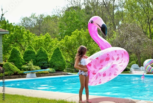 young girl standing next to a pool holding a pink flamingo inflatable