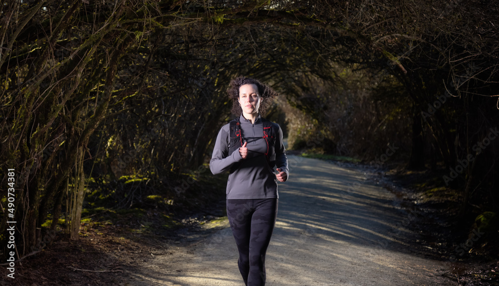 White Caucasian Adult Woman Running on a trail in a Rain Forest. Taken in Surrey, Vancouver, British Columbia, Canada. Sport and Wellness concept White Caucasian Adult Woman Running on a trail in a Rain Forest. Taken in Surrey, Vancouver, British Columbia, Canada. Sport and Wellness concept