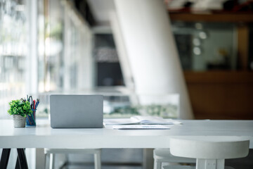 Laptop Computer, notebook, and eyeglasses sitting on a desk in a large open plan office space after working hours