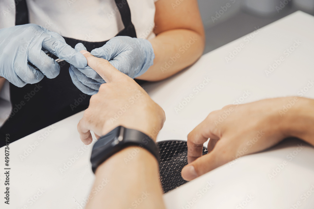 Young man gets professional manicure care for nail in spa salon, white color Young man gets professional manicure care for nail in spa salon, white color