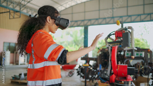 Young Africa American engineer is controlling Futuristic robotic arm with a virtual reality Headset. Testing robot by moving hand at factory. VR Technology industrial and modern equipment.